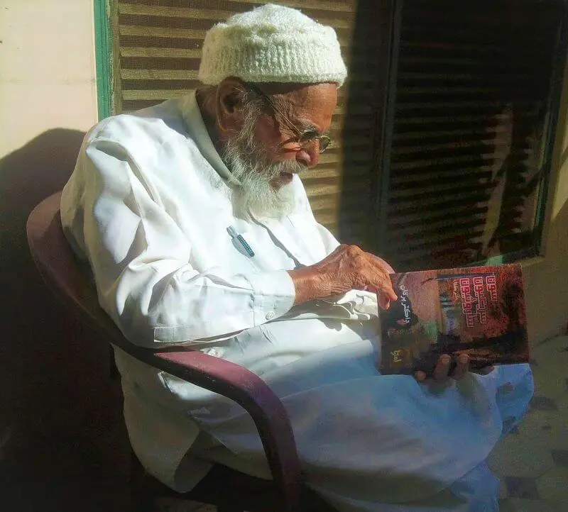 Dr. Harchand Rai Akhani sitting on chair and reading a Sindhi book of author Dr. Pardhan